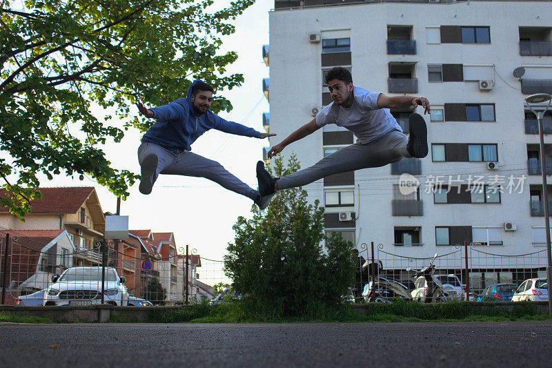 Two white men jumping and stretching their legs in a public park